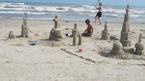 Ein sandiger Strand mit mehreren Sandskulpturen, darunter ein großer Turm und kleinere Bauwerke.