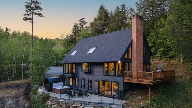 A modern house with a large deck, a hot tub, and a stone foundation.
