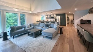 A modern living room with a grey sectional sofa, a coffee table, and a dining area with a long table and chairs.