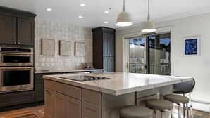 Cocina moderna con una isla grande, electrodomésticos de acero inoxidable e iluminación colgante.