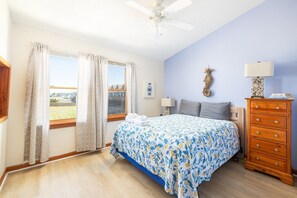 A bedroom with a bed, a dresser, a ceiling fan, and a window with curtains.