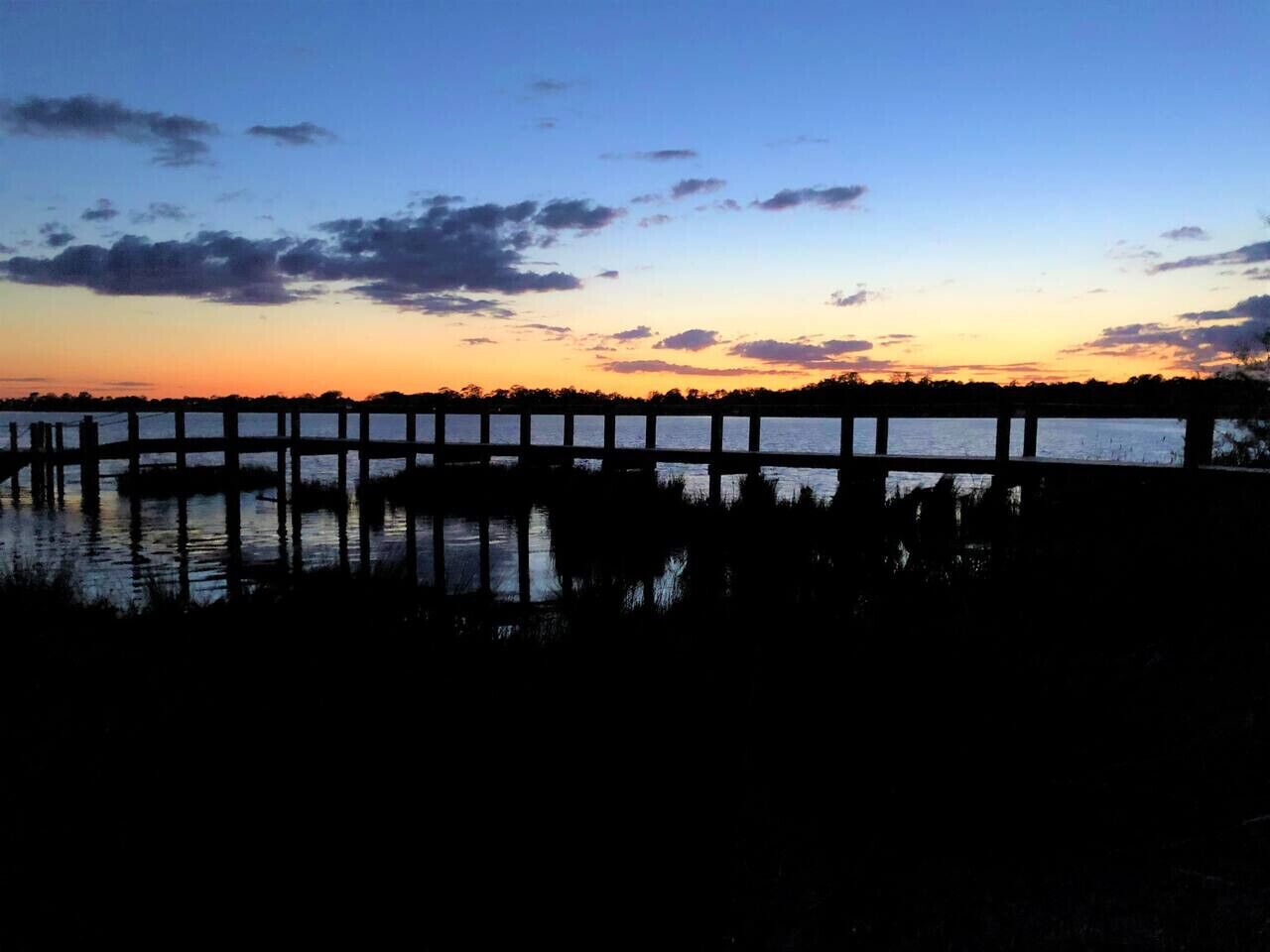Une jetée s’avançant dans l’eau, avec un coucher de soleil en arrière-plan.