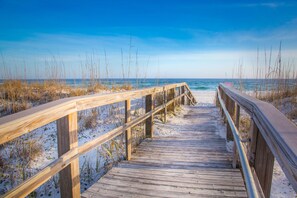 Une promenade en bois qui mène à une plage de sable où la végétation est clairsemée.