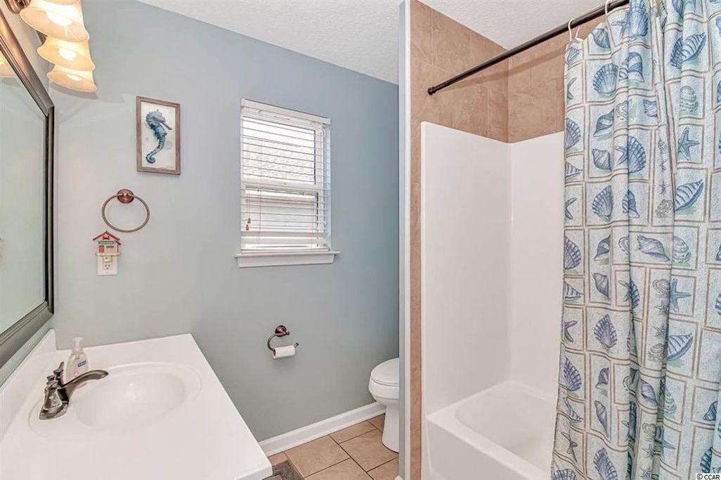 Une salle de bain équipée d’une baignoire, d’un lavabo, de toilettes et d’un rideau de douche orné d’un motif de coquillages.
