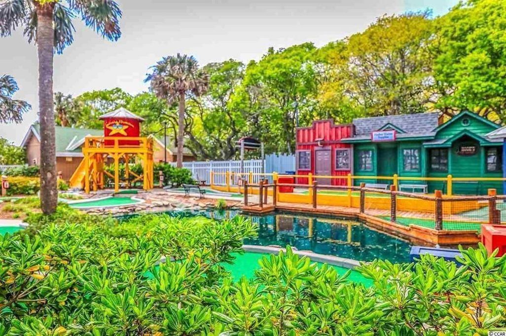 A pool area with a water slide, a lifeguard tower, and a small building with a sign.
