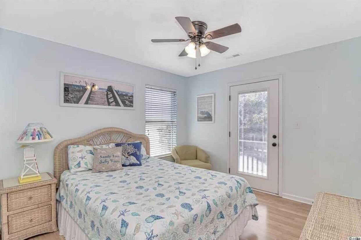 Une chambre à coucher avec un lit, un ventilateur de plafond, une table de chevet, une chaise et une porte.