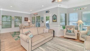 A living room with a beige sofa, two armchairs, a coffee table, and a ceiling fan.