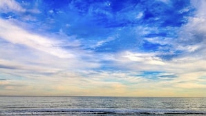 A beach with a view of the ocean and a partly cloudy sky.