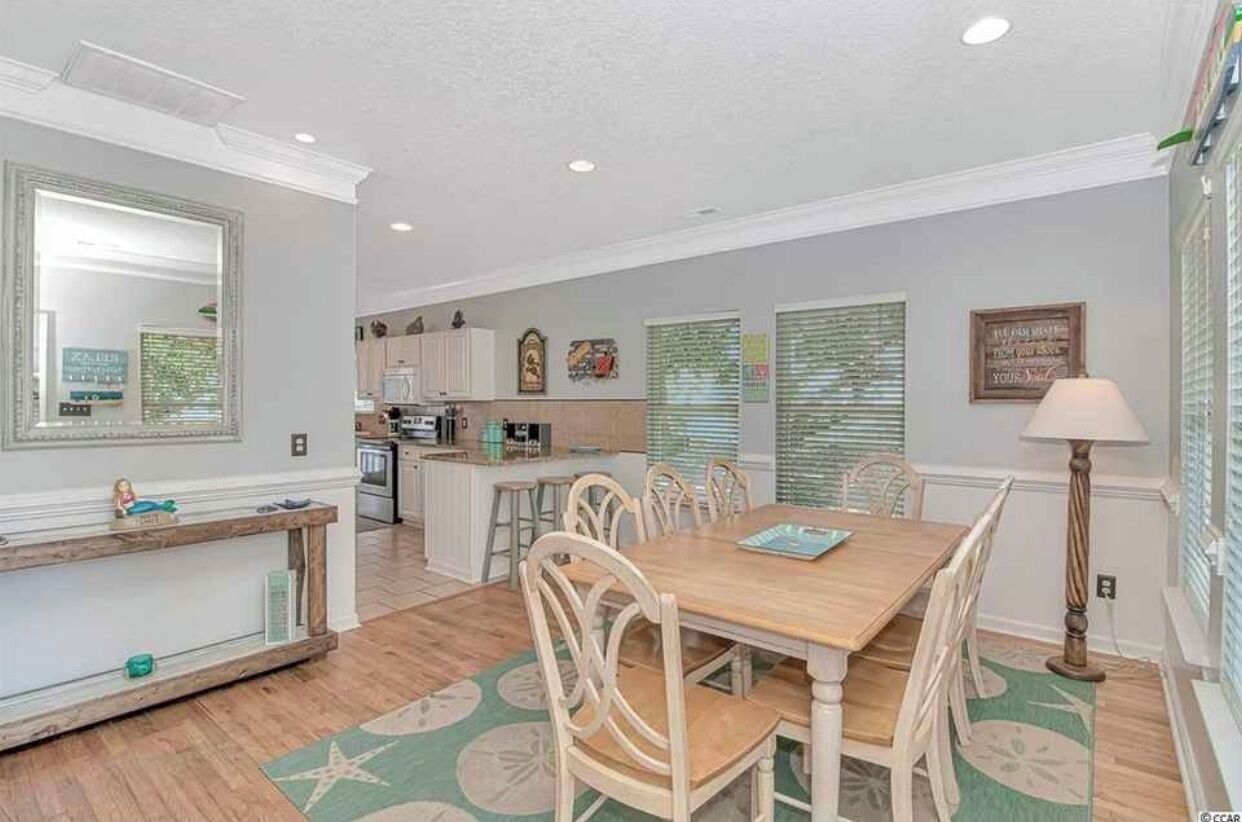 A dining area with a wooden table and chairs, a kitchen in the background, and a floor lamp.