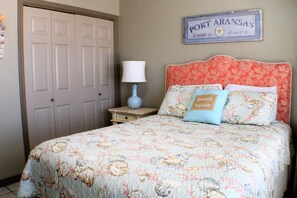 A bedroom with a bed, a nightstand, a lamp, and a wall sign.