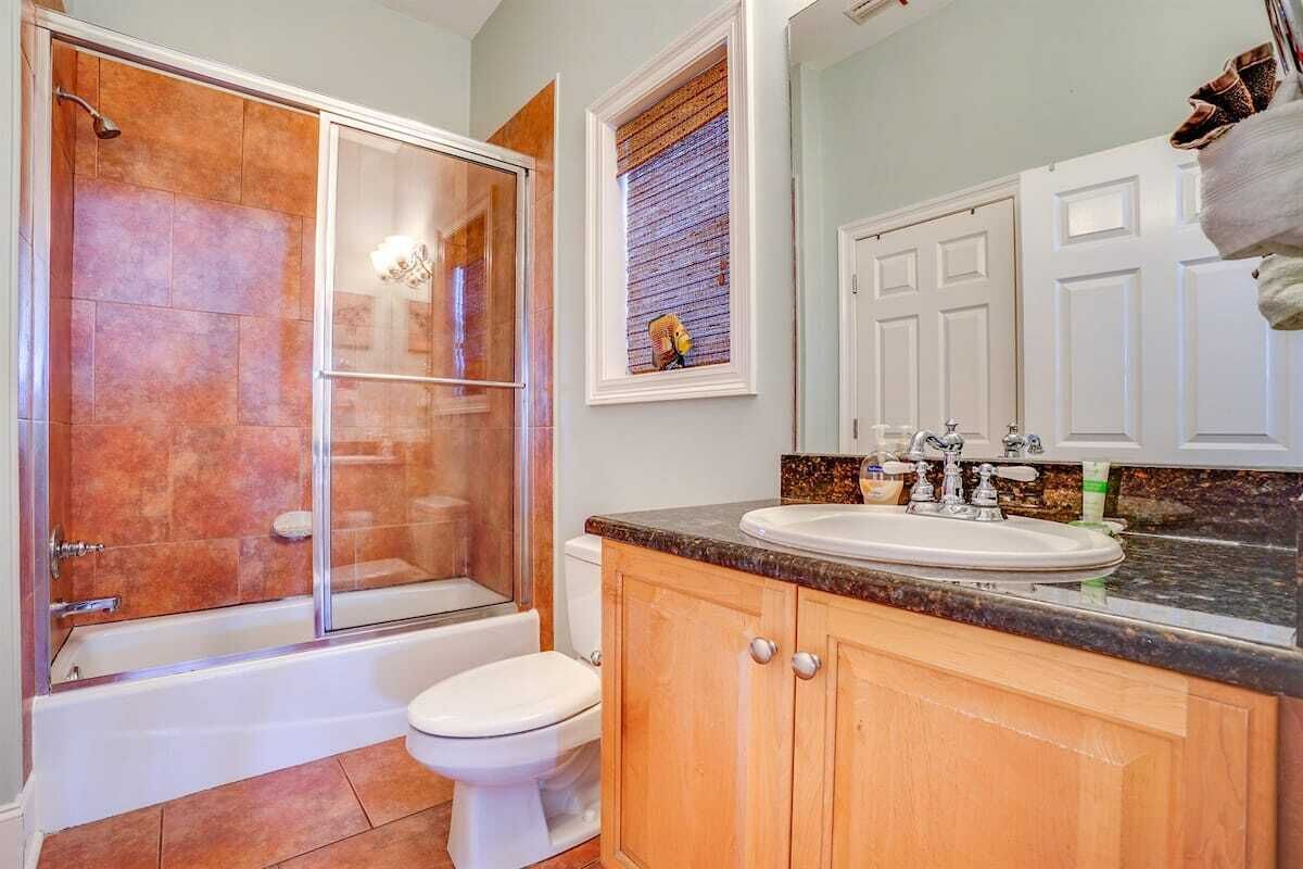 A bathroom with a glass-enclosed shower, a white toilet, a sink with a granite countertop, wooden cabinets, and a mirror above the sink.