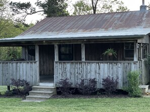 Un bâtiment rustique en bois, doté d’un porche, d’un escalier menant à l’entrée et d’une plante suspendue.