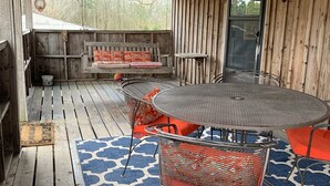 Un terrazzo esterno in legno con un tavolo rotondo e sedie, una panca e un tappeto decorato.