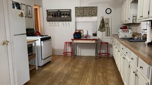 Una cucina con mobili bianchi, pavimento in legno, una ventola a soffitto e una finestra con persiane.