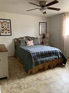 Une chambre à coucher comprenant un lit, une table de chevet, un ventilateur de plafond et des œuvres d’art murales.
