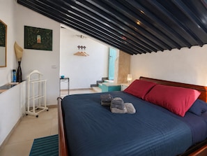 A bedroom with a bed, pillows, a nightstand, a lamp, a small table with a bowl, a hanging garment rack, and a painting on the wall. - Villa Mariani: Villa in San Felice Circeo (San Felice Circeo)