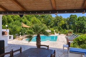Un área de piscina con terraza de madera, sillas de descanso y una palmera.