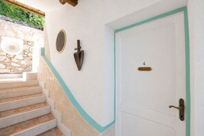 Una puerta blanca con un cartel que dice '4 CABINE', una pared de piedra, un marco de madera y una escalera con azulejos estampados.