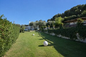 Un'area verde curata con una sfera bianca in primo piano, un muro in pietra e un edificio con tetto in tegole sullo sfondo.