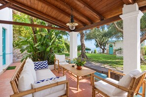 Un espace extérieur aménagé avec une pergola en bois, des coussins blancs et une table agrémentée d’une plante en pot.