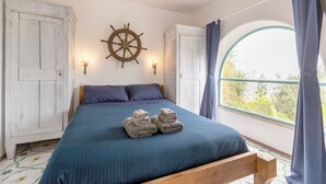A bedroom with a bed, a ship's wheel wall decoration, and a window with curtains.