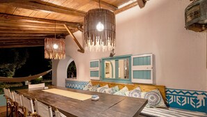 An outdoor dining area with a wooden table and chairs, a hammock, and a bench with patterned cushions.