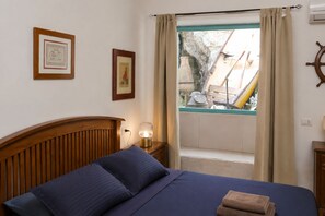 A bedroom with a wooden headboard, a bed with blue bedding, a nightstand with a lamp, and a window with curtains.