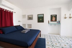 Une chambre d’hôtel avec un lit, un rideau rouge, un climatiseur fixé au mur et un sol carrelé.