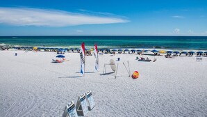 Une plage de sable blanc, avec une eau d’un bleu limpide et plusieurs parasols.