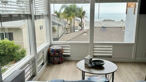 A bedroom with a large bed, a small round table, and a view of the ocean and palm trees through large windows. - San Clemente's "Jewel" - Blue Whale Inn #D (San Clemente)