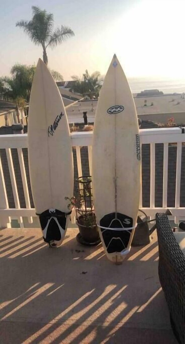 Dos tablas de surf apoyadas en una barandilla blanca con vista a la playa y palmeras.