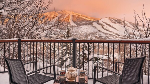 A balcony with two chairs and a table, overlooking a snowy mountain landscape.