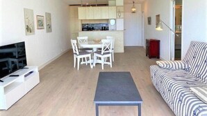 Een moderne woonkamer met een bank, een televisie, een eettafel met stoelen en een keuken in de achtergrond.