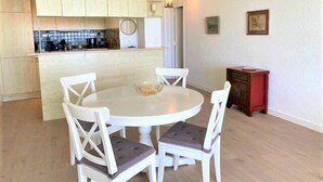 Een eetgedeelte met een ronde tafel en vier stoelen, een keuken met houten kasten, en een klein rode kast.