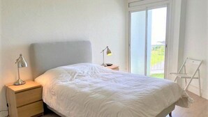 Een slaapkamer met een bed, twee nachtkastjes, een raam en een stoel.
