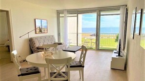 Een eethoek met een ronde tafel en stoelen, een gestreepte bank en een balkon met uitzicht op zee.