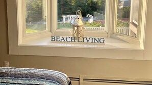 Une chambre avec une grande fenêtre donnant sur une plage, une décoration en forme d’étoile de mer et une pancarte indiquant « VIVRE AU BORD DE LA PLAGE ».