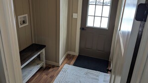 Un couloir étroit avec un banc en bois, une porte dotée d’une fenêtre et une petite étagère.