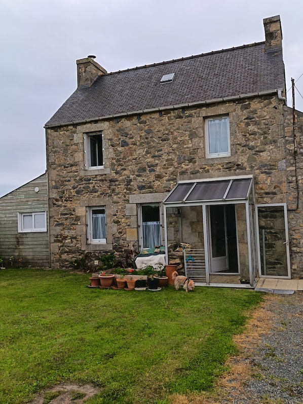 A stone house with a sloped roof, a glass door entrance, and a small lawn with potted plants.