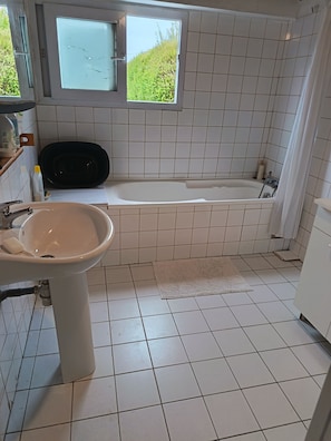 A bathroom with a sink, a bathtub, and a window with a view of greenery.