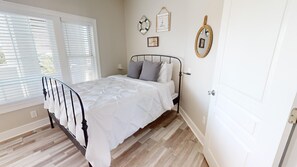 A bedroom with a bed, wooden flooring, a window with blinds, and wall decorations.
