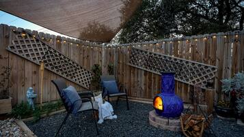 A patio area with a wooden fence, outdoor seating, a blue fire pit, and string lights.