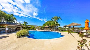 Un área de piscina con sillones de descanso, una zona de barbacoa y una sombrilla de paja.