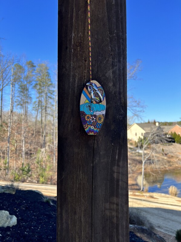 A wooden post with a colorful, patterned object hanging from it. - New! Lakefront with Views from Every Window - With Dock, Fire Pit, BBQ, Kayaks (West Union)