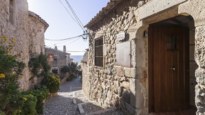 Une étroite rue pavée, bordée de bâtiments en pierre, avec une porte en bois et une enseigne indiquant une villa nommée « Villa Pandora ».
