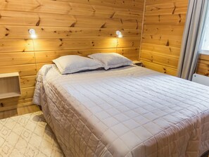 A wooden-paneled room with a bed, two bedside lamps, and a nightstand.