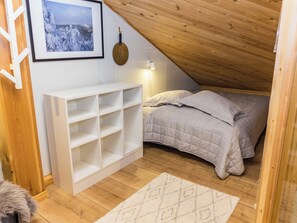 Una camera da letto mansardata accogliente con un letto, un ripiano bianco, un quadro incorniciato e una lampada.