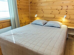 Un letto con un piumone bianco trapuntato, due cuscini e una testiera in legno con due luci a parete.