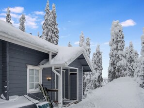 Una casa cubierta de nieve con un porche y un soporte para esquíes afuera.