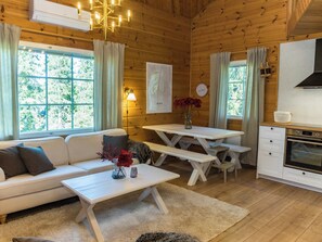 Interior acolhedor de uma cabana, com um sofá, uma mesa de jantar e uma cozinha compacta.
